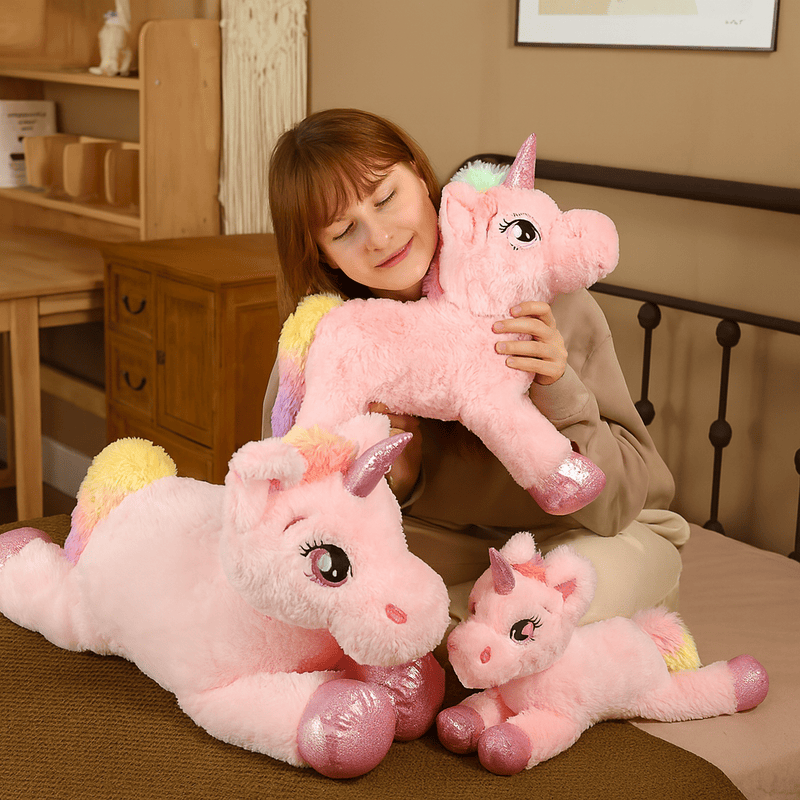 Trois peluches licornes rose sur un lit avec une fille