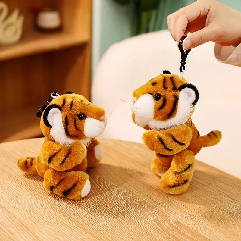 Deux mini peluches tigres orange sur une table avec une fille qui en tient une par la ficelle