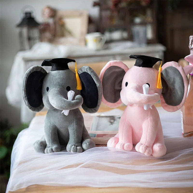 Deux peluches éléphants rose et grise diplômé sur une table avec une toile de robe