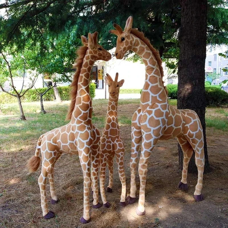 Trois peluches girafes xxl dans la nature devant un arbre