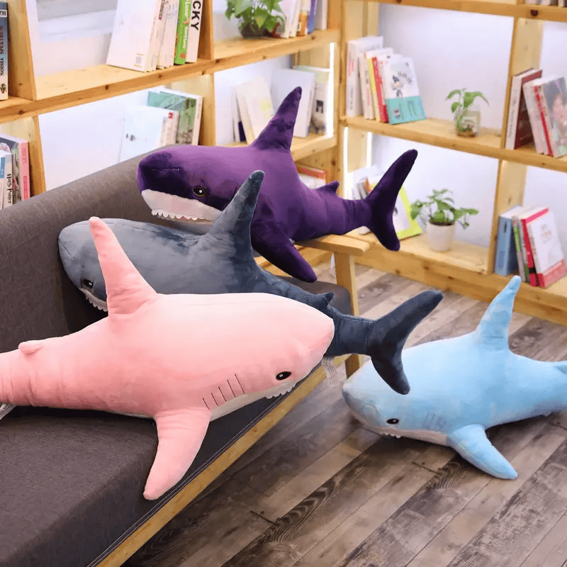 Quatre peluches requins sur un canapé dont une peluche requin par terre