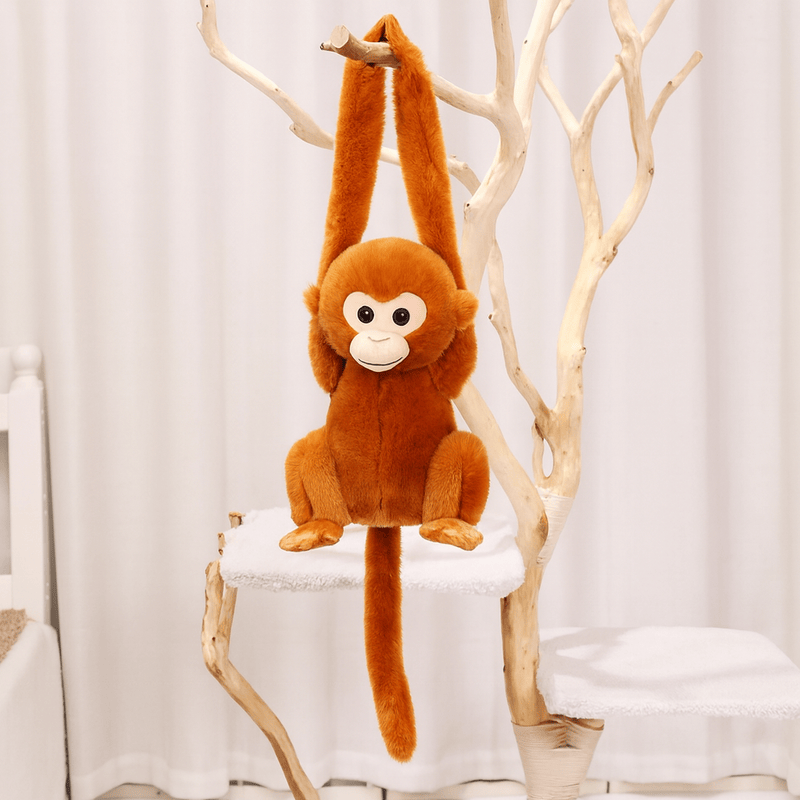 Peluche singe aux poils roux avec la tête blanche suspendu par les bras sur un arbre en intérieur Image