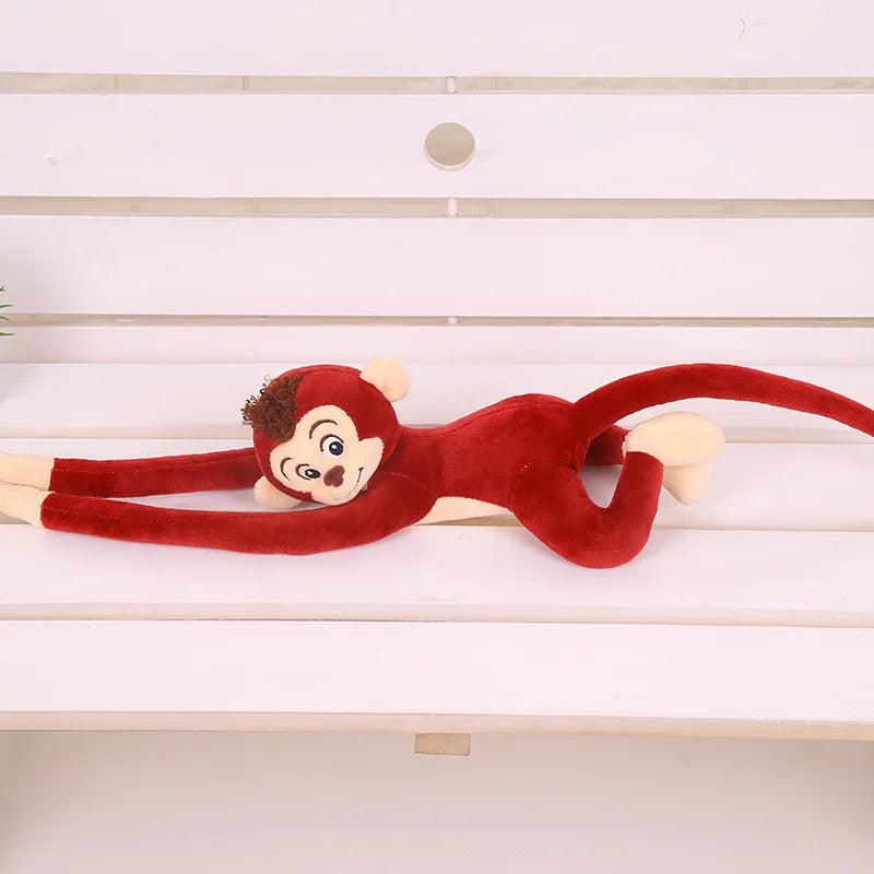 Peluche singe rouge suspendu couché sur un banc