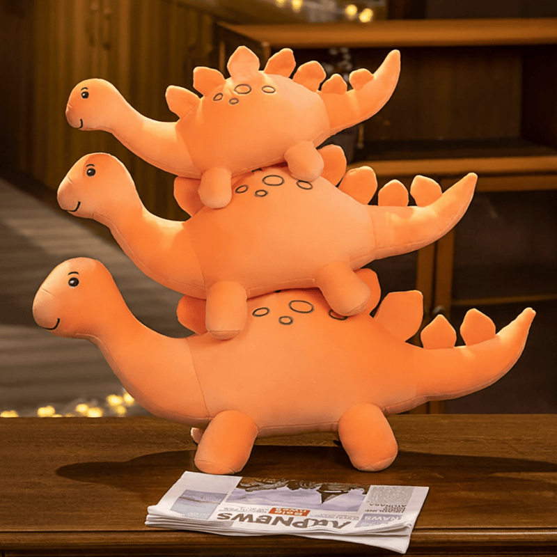 Trois peluches stégosaure orange sur une table