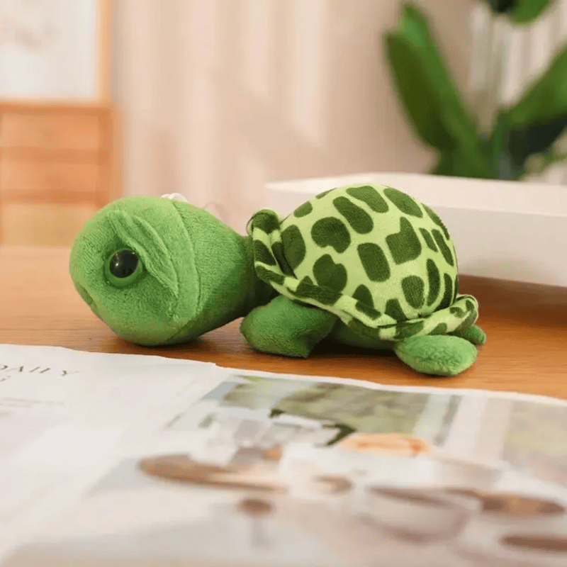 Peluche tortue gros yeux de profil sur une table avec un magazine 