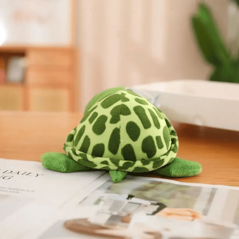 Peluche tortue gros yeux de dos sur une table avec un magazine 