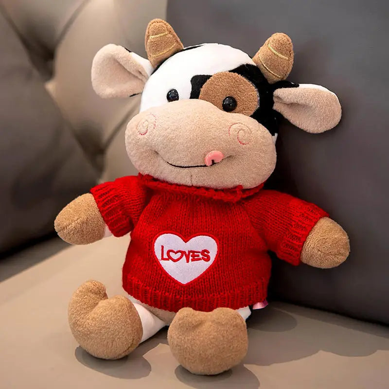 Peluche vache avec son col roulé rouge avec un coeur sur un canapé