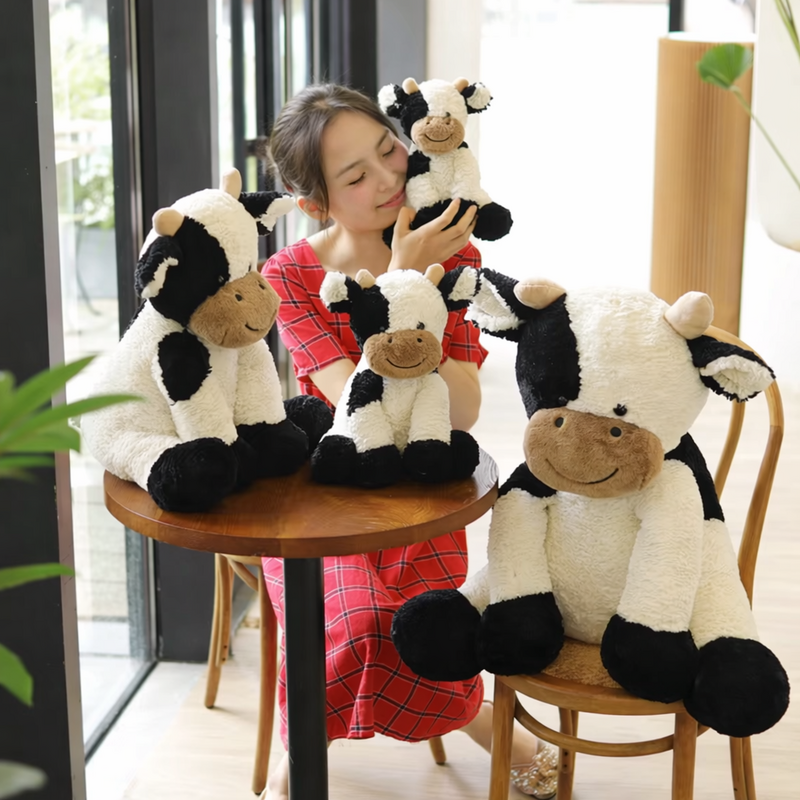 Quatre peluches vaches kawaii avec une femme sur une chaise et une table ronde 