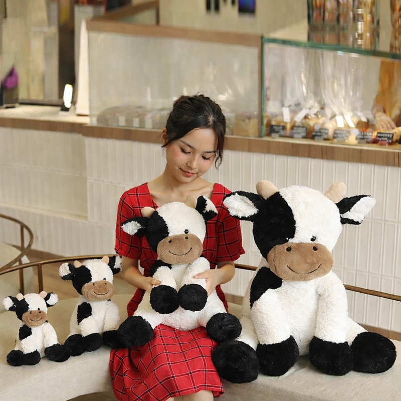 Quatre peluches vaches kawaii avec une femme sur un canapé dont une vache assise sur la femme